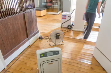Air mover and dehumidifier drying a water-damaged floor